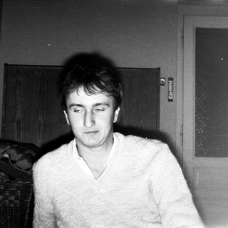 Young man indoors, wearing sweater, looking downward.