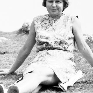 Woman sitting outdoors in floral dress, mid-20th century.