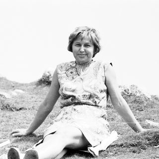 Woman sitting outdoors in floral dress, mid-20th century.