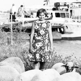 Girl standing with herd of sheep outdoors.