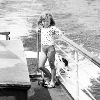 Young girl smiling on boat railing near water.