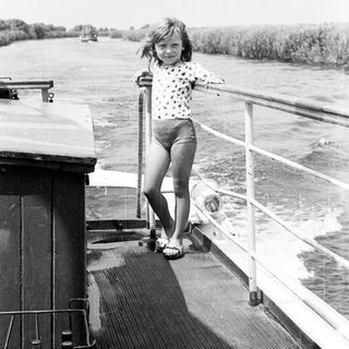 Young girl standing on boat railing near water.