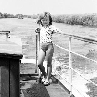 Young girl standing on boat railing near water.