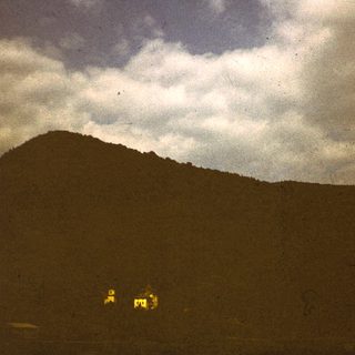 Dark mountain landscape with storm clouds, illuminated by distant lights.