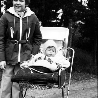 Young boy pushing baby stroller outdoors.