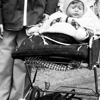 Young boy pushing baby stroller outdoors.