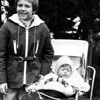 Young boy pushing baby stroller outdoors.