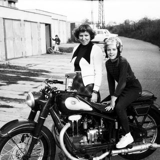 A woman and child pose on a vintage motorcycle.