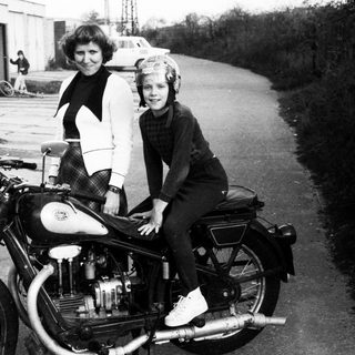 A woman and child pose on a vintage motorcycle.