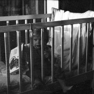 Child peeking through crib bars indoors.