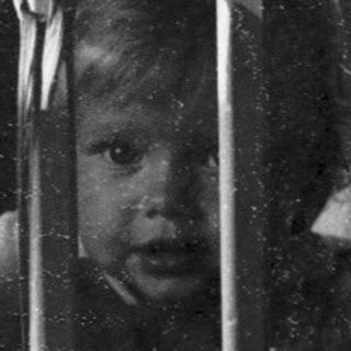 Child peeking through crib bars indoors.