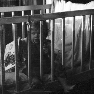 Child peeking through crib bars indoors.