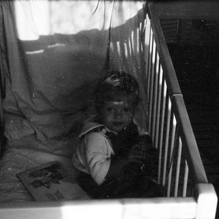 Child peeking cautiously from inside a crib.