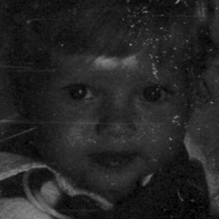 Child peeking cautiously from inside a crib.