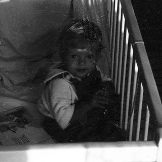 Child peeking cautiously from inside a crib.