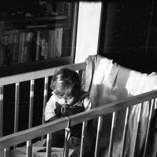 Child sitting in crib, peering through bars.