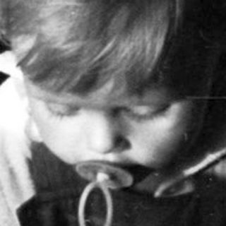 Child sitting in crib, peering through bars.