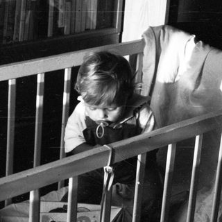 Child sitting in crib, peering through bars.