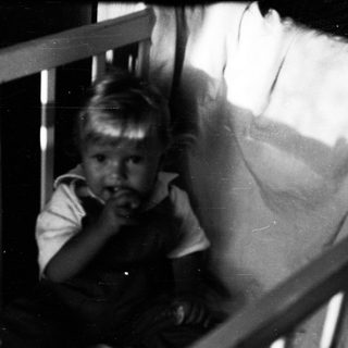 Young child peering through crib bars.
