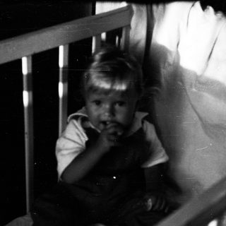 Young child peering through crib bars.