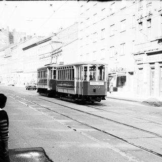 Vintage streetcar on urban roadway with pedestrians.