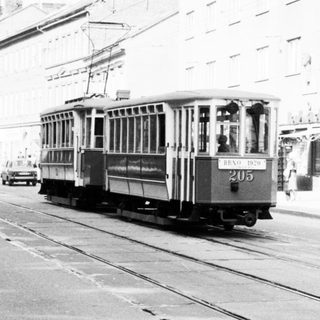 Vintage streetcar on urban roadway with pedestrians.