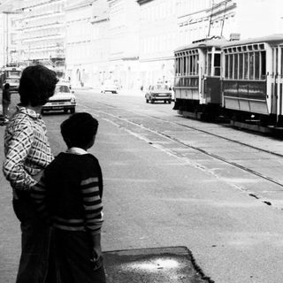 Vintage streetcar on urban roadway with pedestrians.