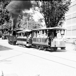 Vintage steam-powered tram with passengers on city street.