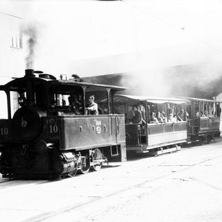Steam locomotive train with passengers in vintage station setting.