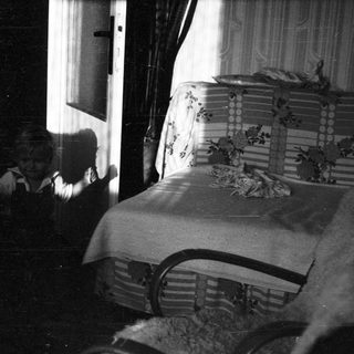 Vintage bedroom with bed, curtains, and shadowy figure.