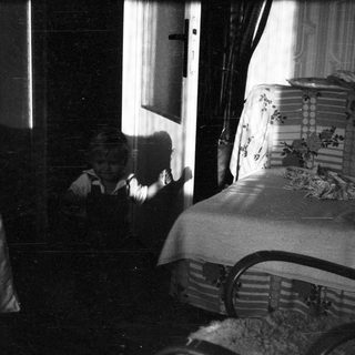 Vintage bedroom with bed, curtains, and shadowy figure.