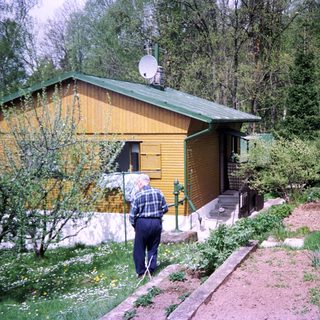 Small wooden house in rural garden area. Elderly person gardening.