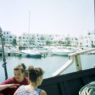 Two women on boat near marina with yachts.
