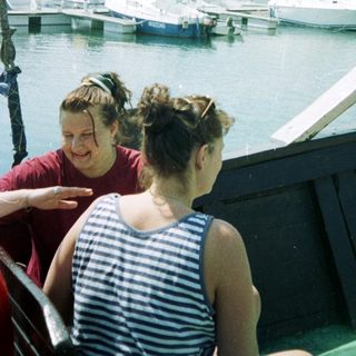 Two women on boat near marina with yachts.