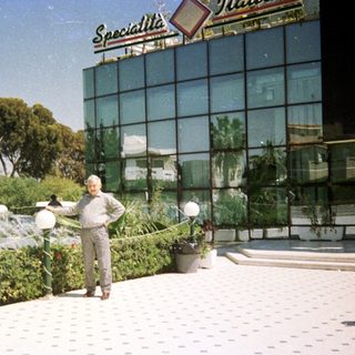 Man watering plants near modern building.