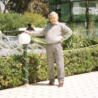 Man watering plants near modern building.