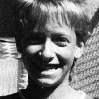 Young boy smiling outside near window.