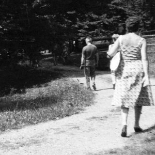 Small wooden hut in forested area with two people walking.