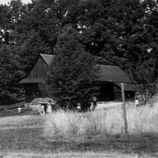 Rural open-air museum with traditional wooden buildings and visitors.
