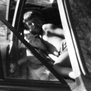 Two people in a parked vintage car.