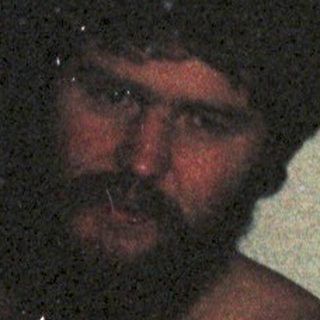 Shirtless man in dim lighting, wearing low-slung pants.
