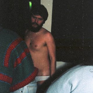 Shirtless man in dim lighting, wearing low-slung pants.