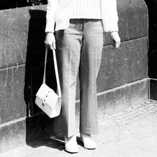 Woman standing outdoors near stone wall holding bag.