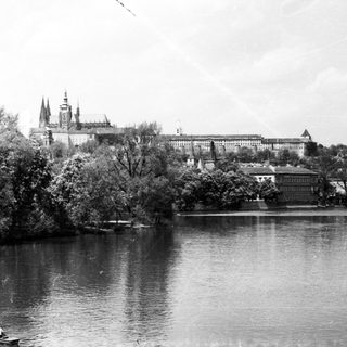 Historic castle complex by river with cathedral spires.