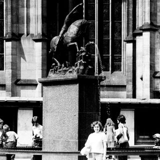 Woman standing beside equestrian statue in city plaza.