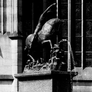 Woman standing beside equestrian statue in city plaza.