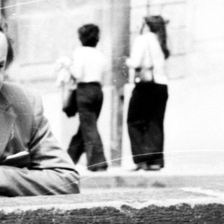 People gathered outdoors near brick wall in 1970s-style setting.