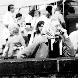 People gathered outdoors near brick wall in 1970s-style setting.