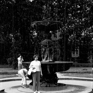 People posing near ornate fountain in park.