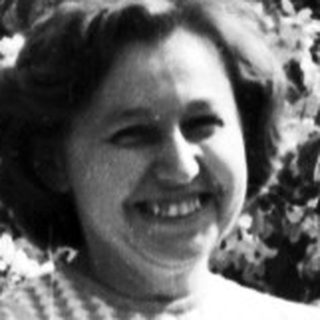 Woman smiling outdoors holding shopping bag.